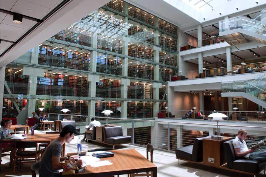 A bright study area inside Thompson Library with tables beside the glass stacks tower.